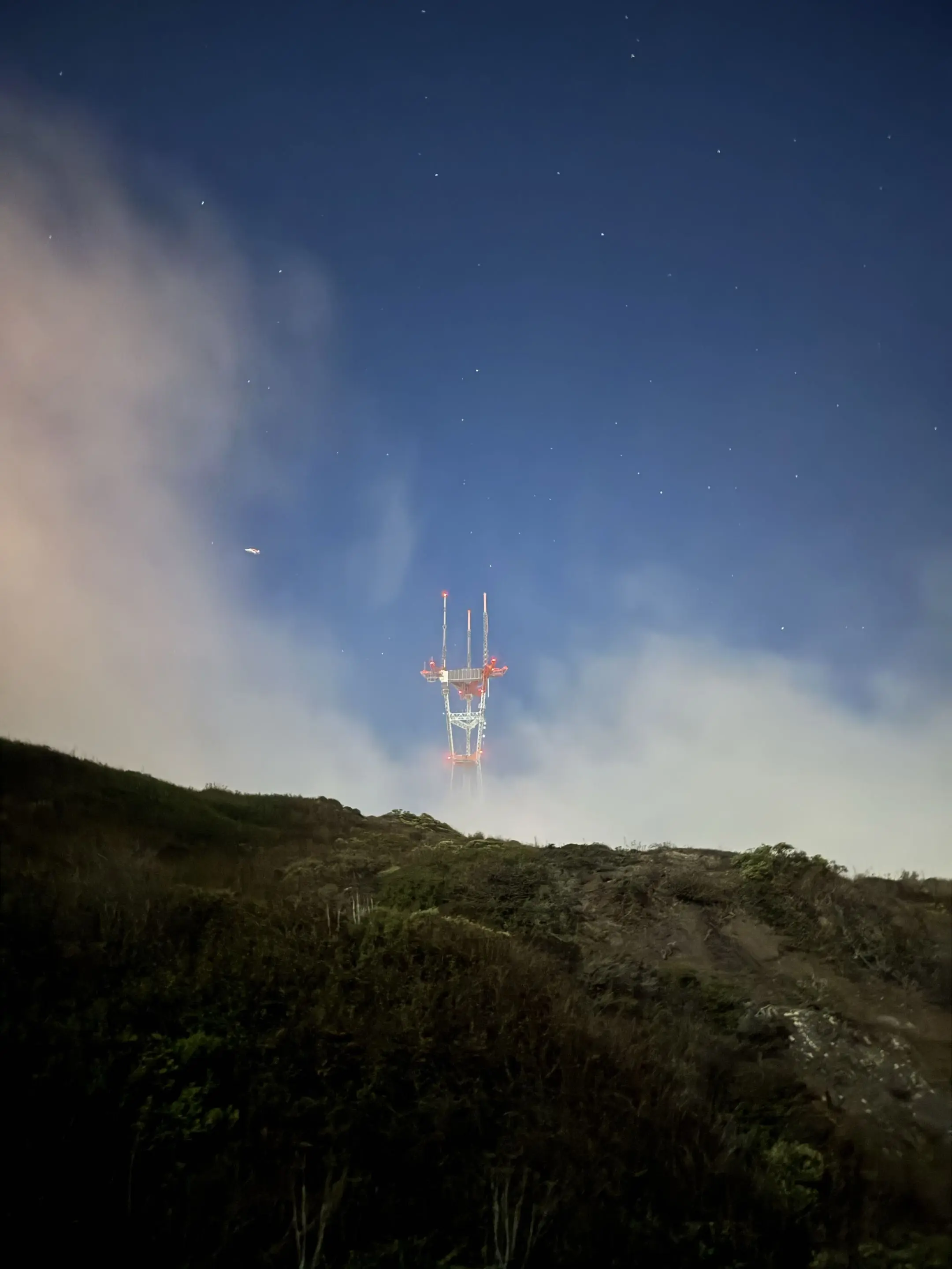 Twin towers glowing at night against a clouded mountain sky.