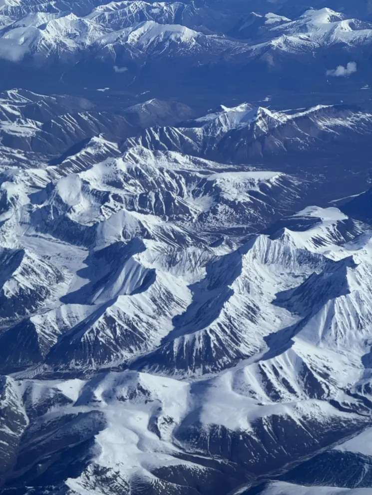 Aerial view over snow-dusted blue mountain ranges fading into the distance.